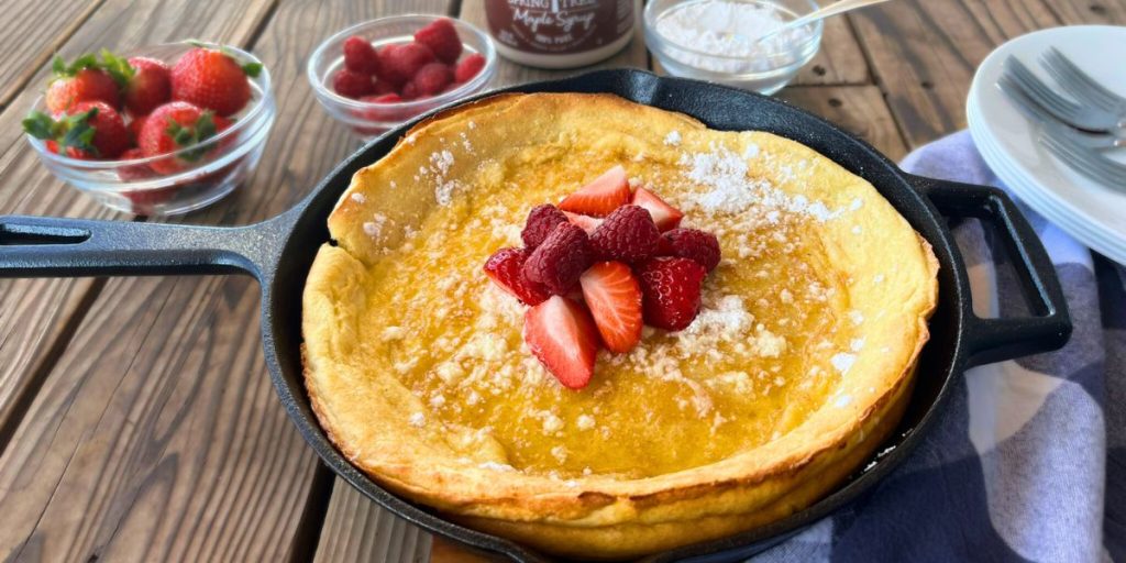 a high altitude Dutch baby pancake in a cast iron skillet with fresh raspberries and strawberries piled in the middle