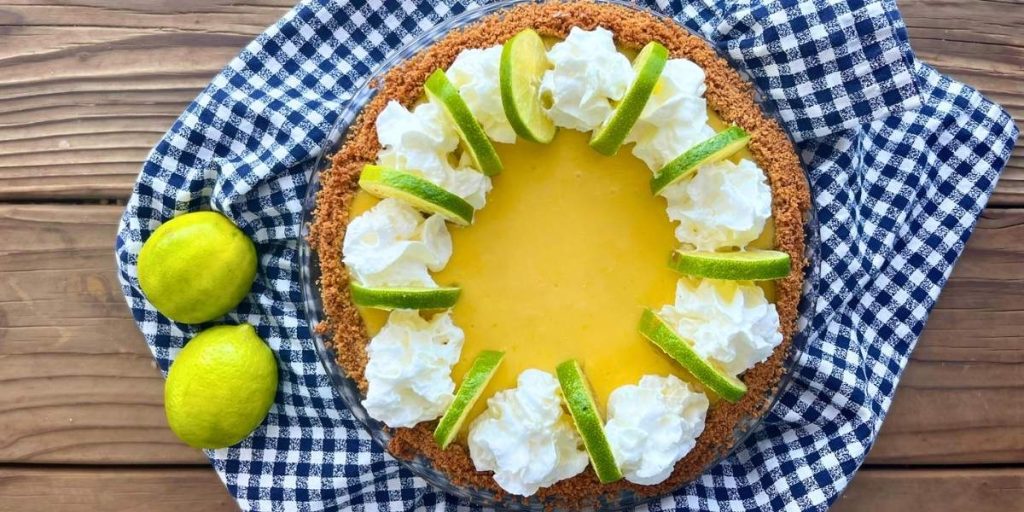 a whole high altitude key lime pie with fresh dollops of whipped cream and key lime slices alternating around the outer edge