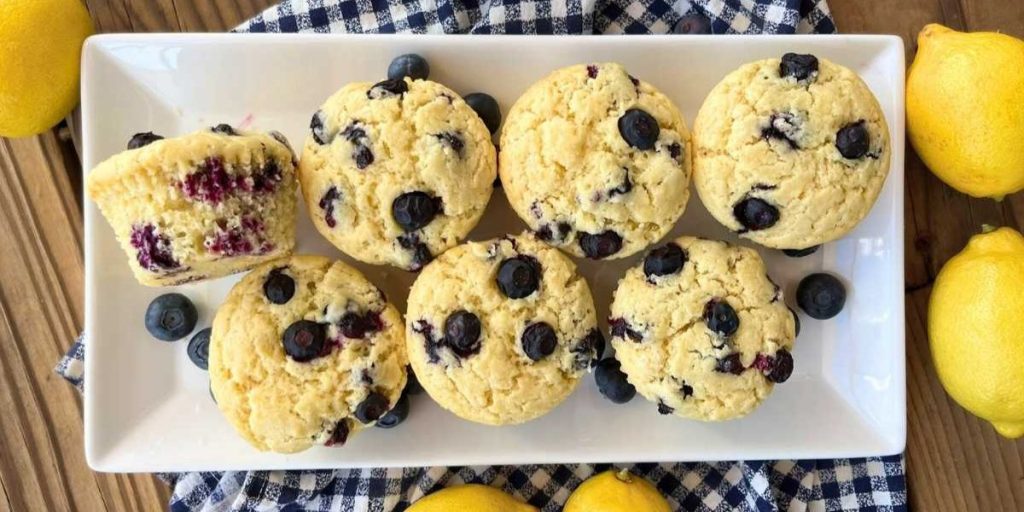 7 lemon blueberry muffins laid out of a white serving platter surrounded by fresh lemons