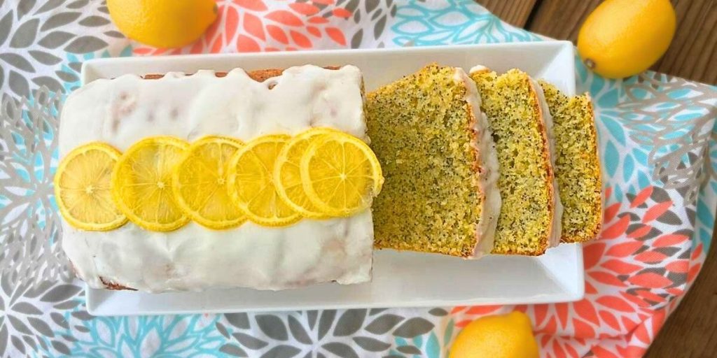 a loaf of high altitude lemon poppy seed bread topped lemon glaze icing with 3 slices cut off