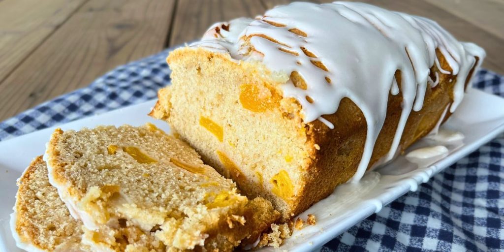a loaf of high altitude peach bread with peach icing with 2 slices cut off laying on a white serving platter