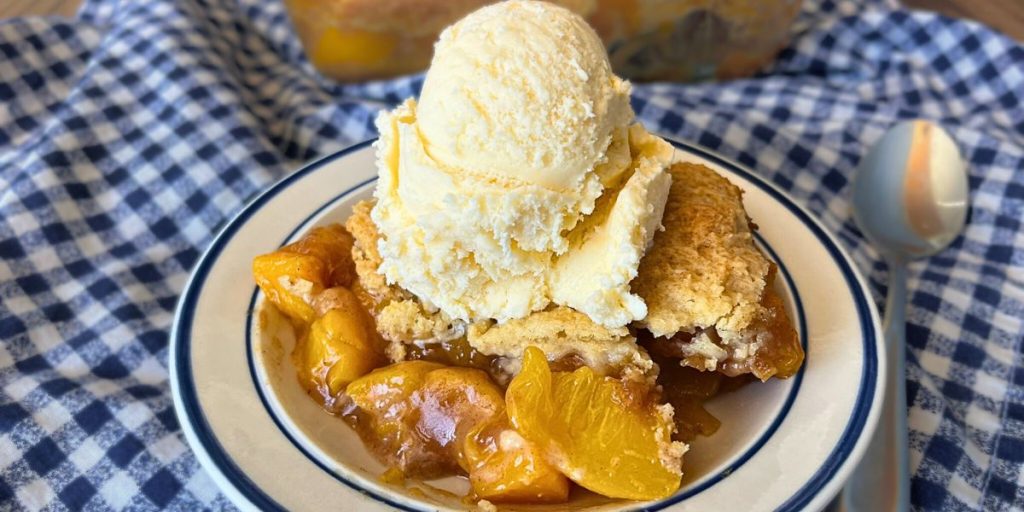 1 serving of southern style high altitude peach cobbler on a white and blue plate with a large dollop of vanilla ice cream on top