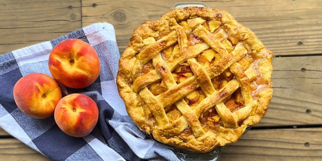 whole high altitude peach pie with 3 fresh peaches sitting next to it