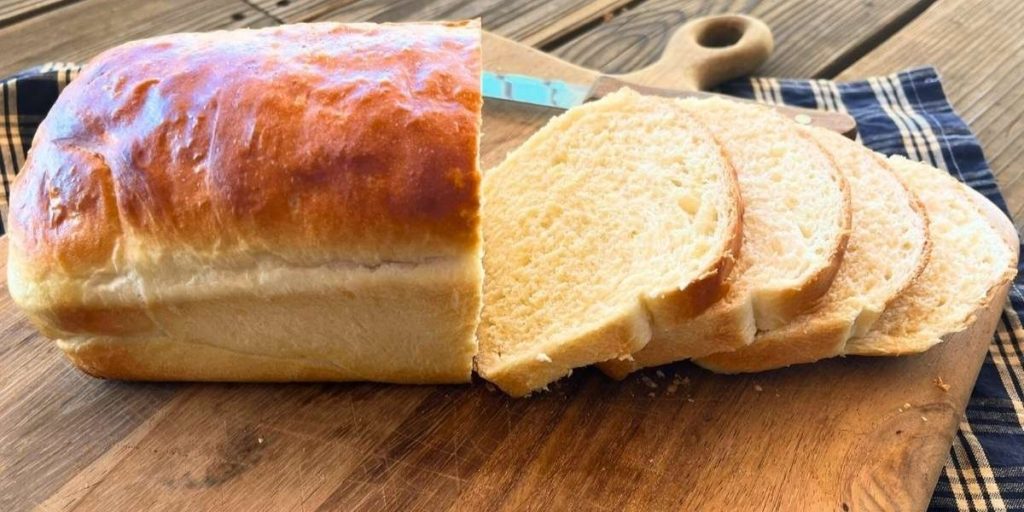 a loaf of high altitude white sandwich bread with 4 slices cut off laying on a cutting board