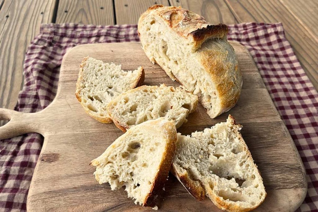 high altitude sourdough bread with 4 slices sitting on a wood cutting board