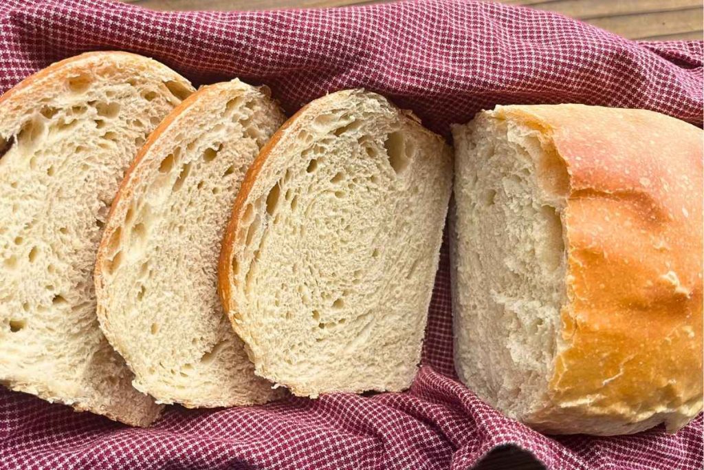 A loaf of high altitude sourdough sandwich bread with 3 slices cut off in a bread basket.