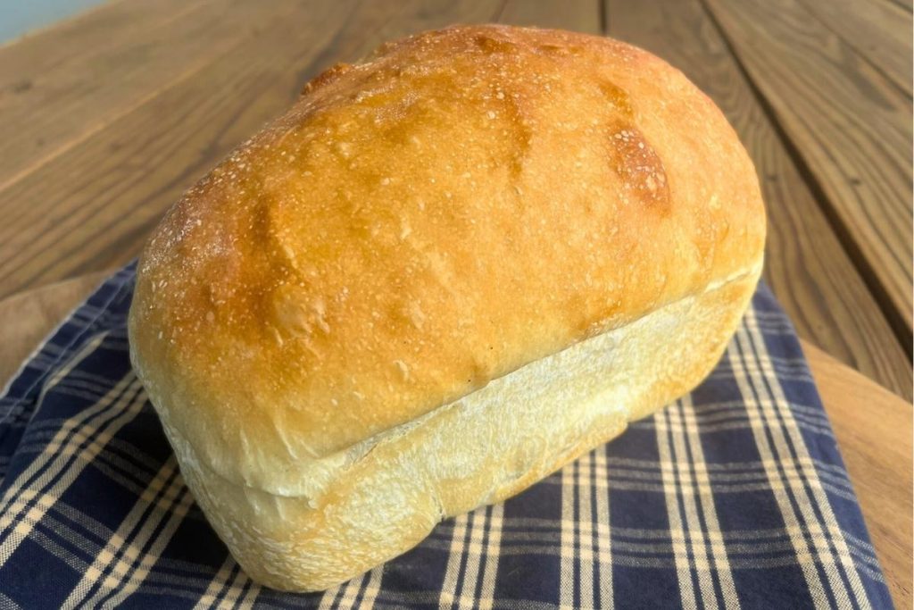 a loaf of high altitude sourdough sandwich bread sitting on a tea towel and wood cutting board