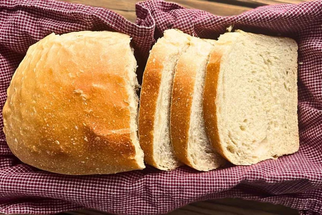 A loaf of high altitude sourdough sandwich bread with 3 slices cut off in a bread basket.