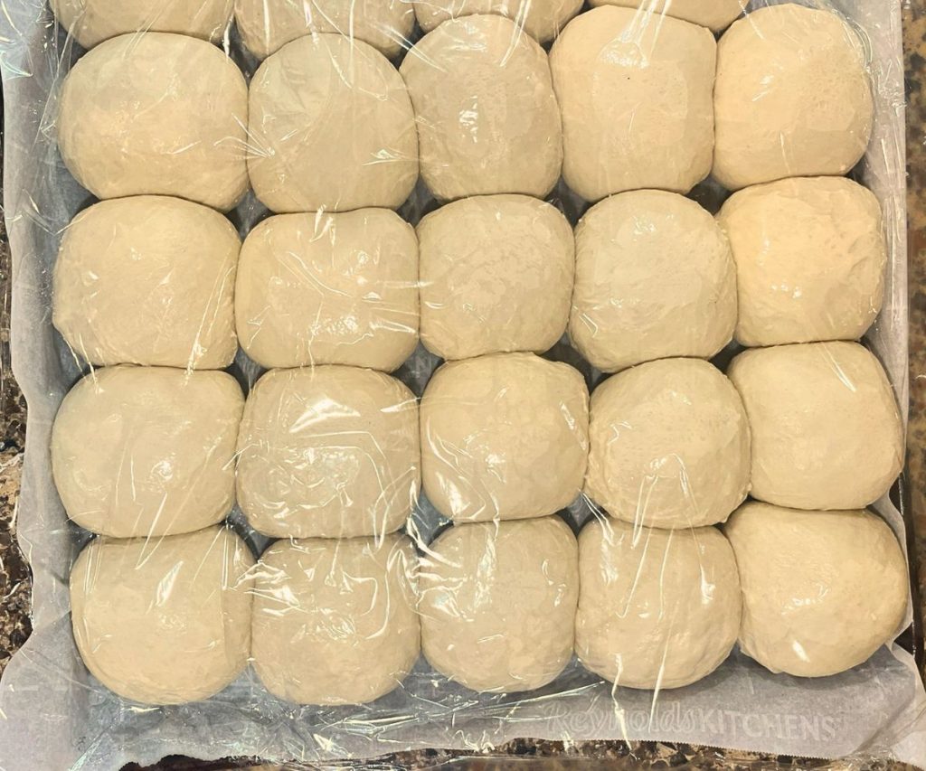 a baking dish with sourdough dinner rolls covered with plastic wrap during the final rest