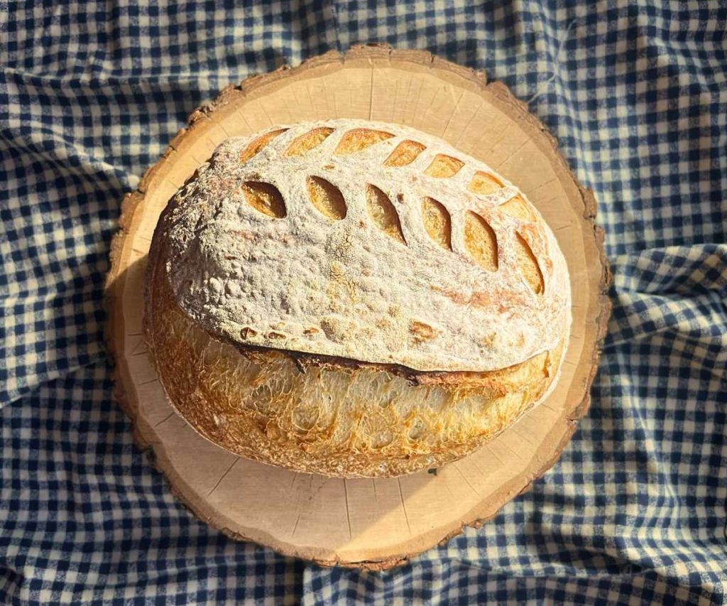 a loaf a high altitude sourdough bread on a wood slice on a blue and white tea towel
