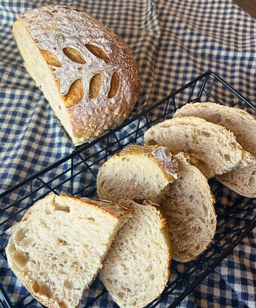 slice of high altitude sourdough bread in a bread basket next to the whole loaf