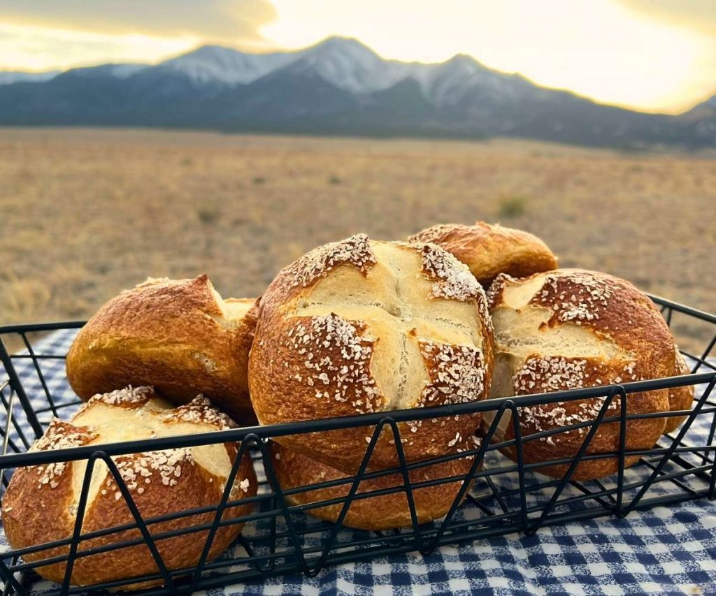 a basket of high altitude pretzel buns on a tablecloth in front of the Colorado Rocky Mountains