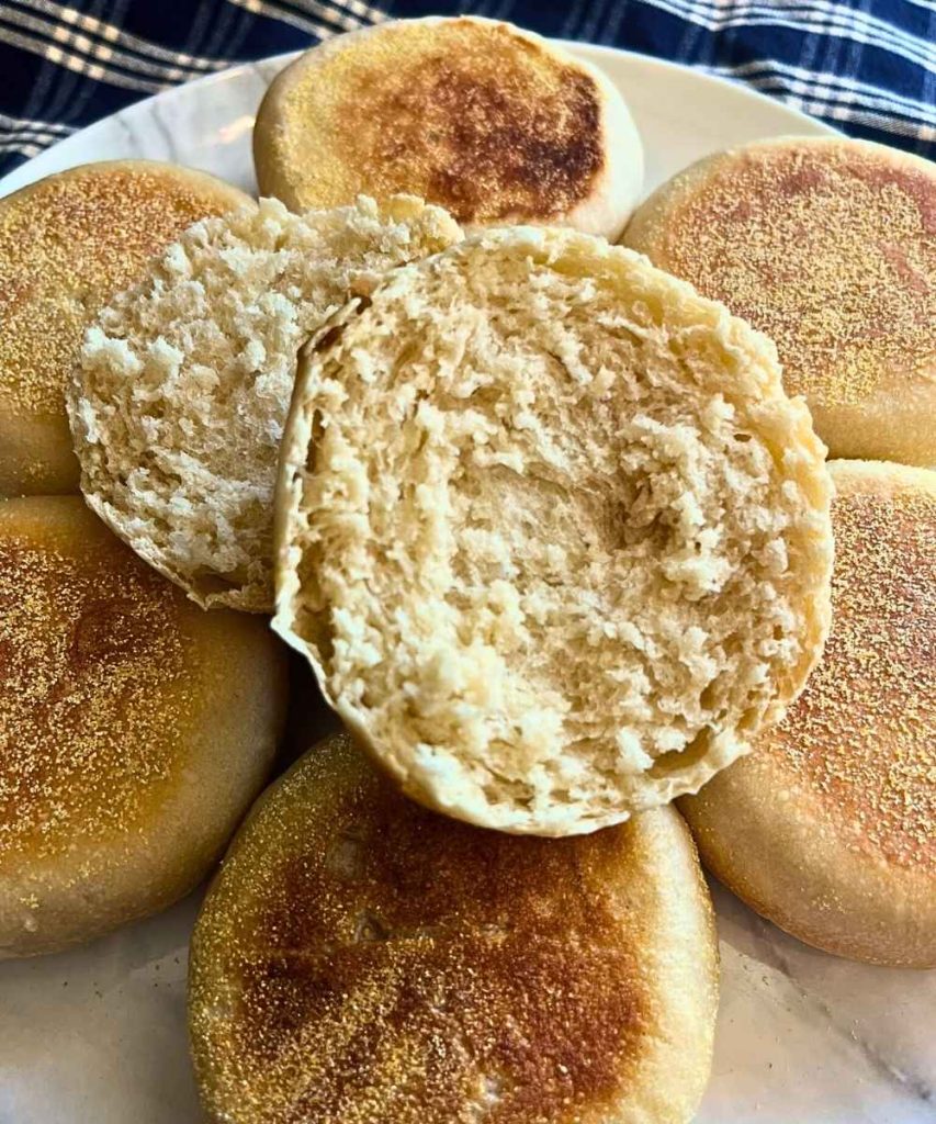 a plate full of high altitude sourdough English muffins with one cut in half
