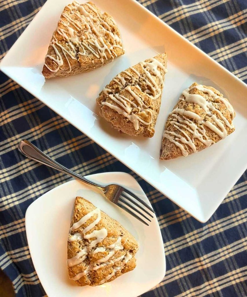 3 cinnamon roll scones on a white platter on top of a white and blue table clothe
