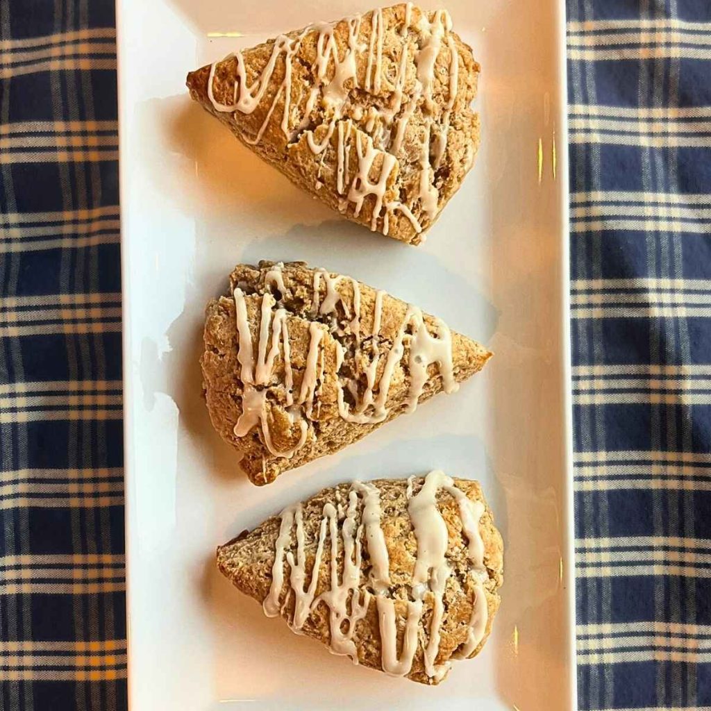 3 cinnamon roll scones on a white platter on top of a white and blue table clothe