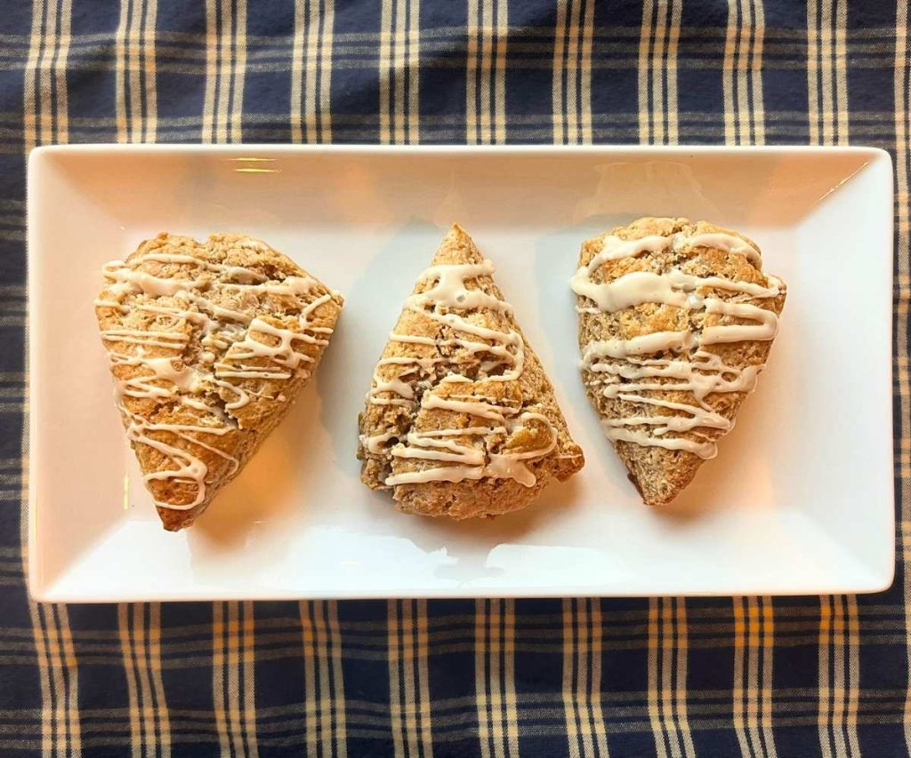 3 cinnamon roll scones on a white platter on top of a white and blue table clothe