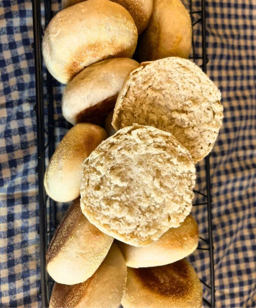 a basket full of high altitude sourdough English muffins with one cut in half