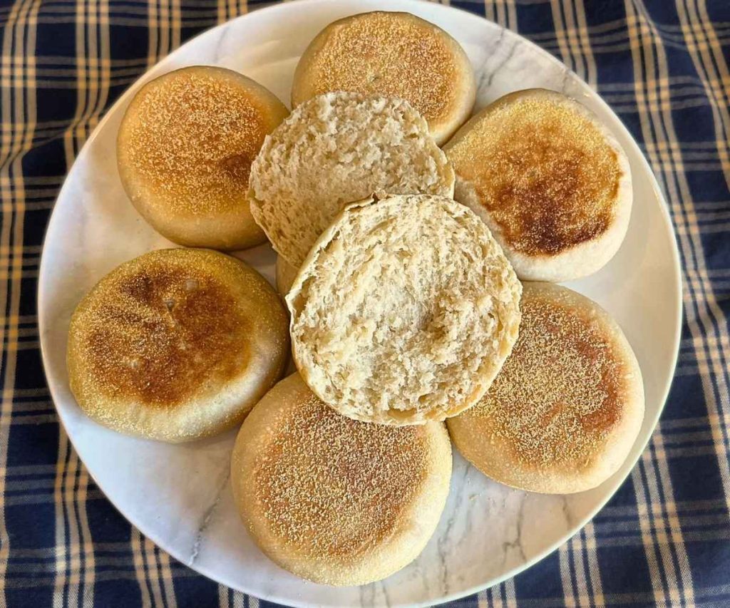 a plate full of high altitude sourdough English muffins with one cut in half