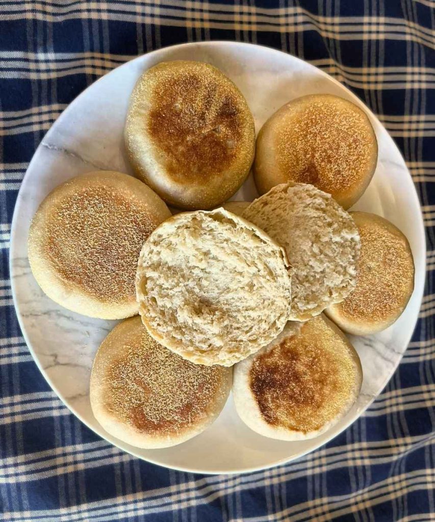 a plate full of high altitude sourdough English muffins with one cut in half