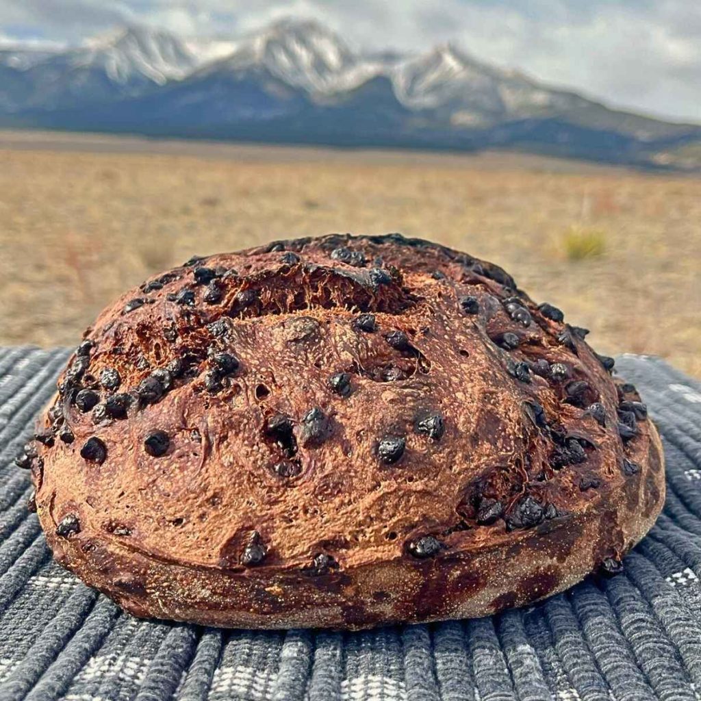 a loaf of sourdough double chocolate artisan bread on a table in front of the Colorado Rocky Mountains